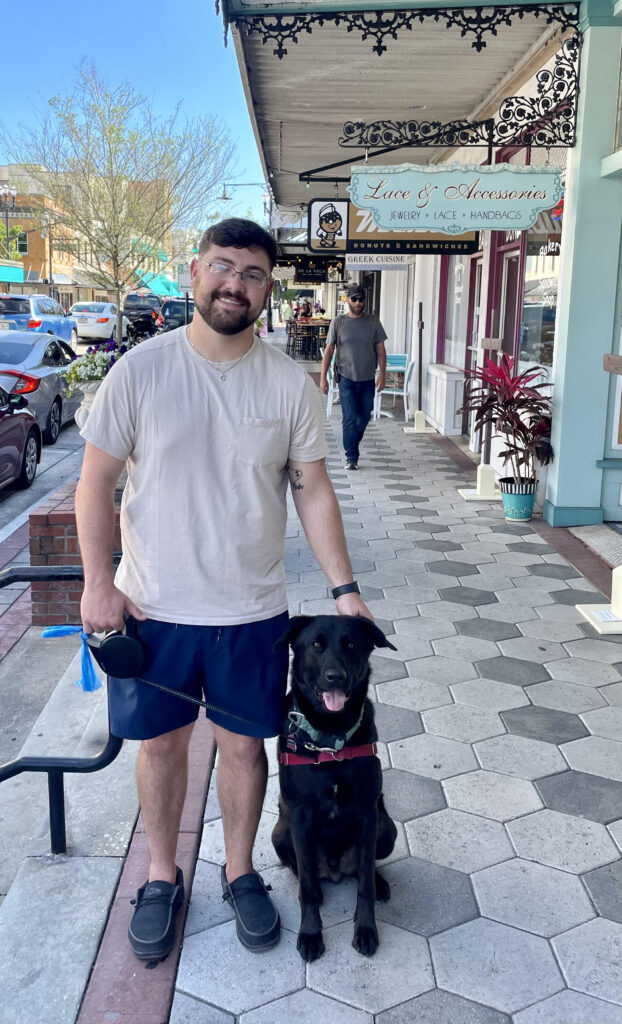 A man and his dog are standing on the sidewalk.