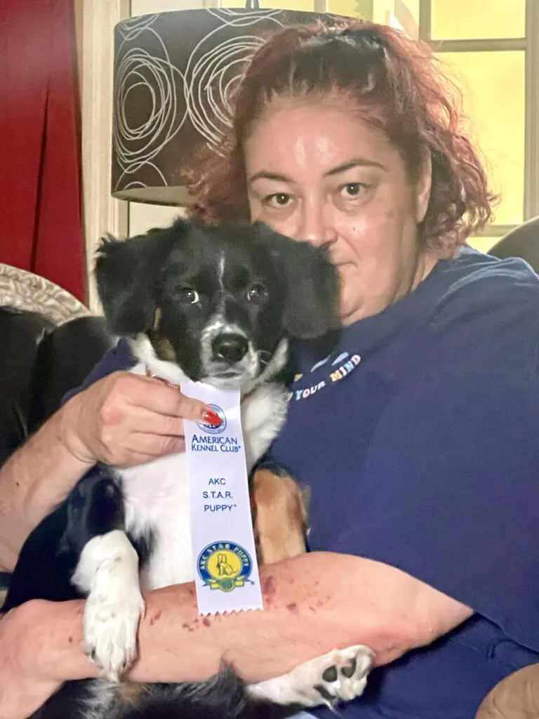 A woman holding a dog with a ribbon around its neck.