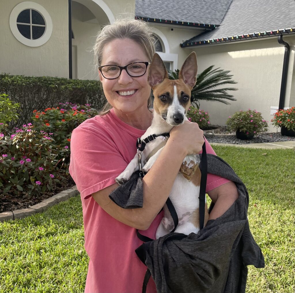 A woman holding her dog in front of a house.